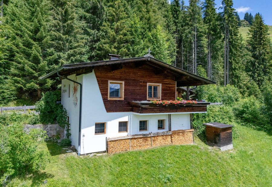 Bergchalet mit Holzbalkon und Blumen, umgeben von Wiese und Wald