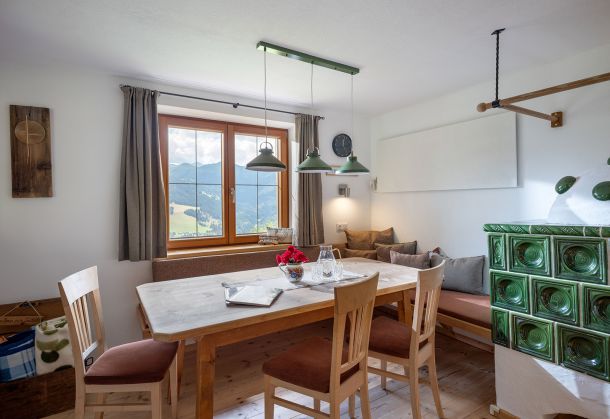 Gemütliche Stube mit Esstisch, Eckbank, grünem Kachelofen und Bergblick