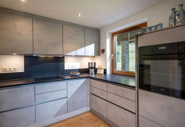 Moderne Küche mit grauen Fronten, dunkler Arbeitsplatte und großem Fenster