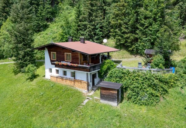 Bergchalet in Alleinlage auf einer grünen Wiese zwischen bewaldeten Berghängen
