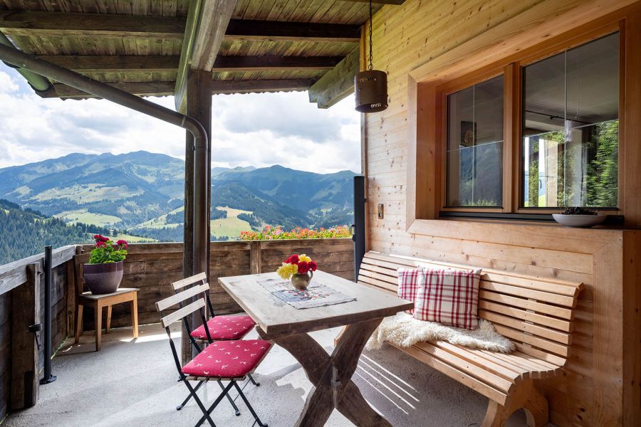 Überdachte Holzterrasse mit Tisch, Sitzbank und Blick auf eine Berglandschaft